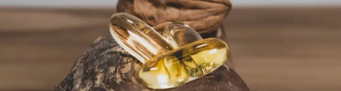 Trois capsules d'oméga 3 dorées reposent sur une noix. Quand prendre oméga 3 pour un bien-être optimal ?