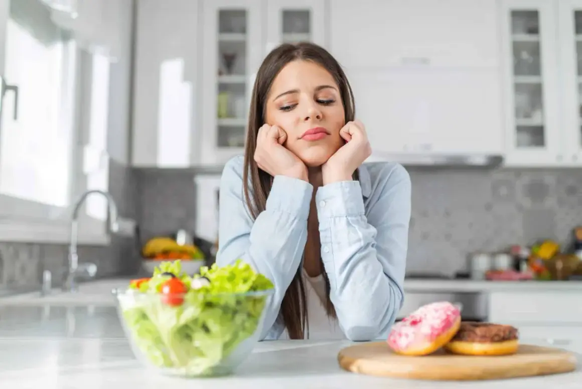 Une jeune femme dépitée face à une salade et des donuts, symbolisant le dilemme des aliments à éviter pour la dermite séborrhéique.
