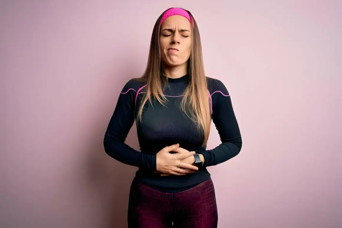 Femme en tenue de sport, mains sur le ventre, grimace de douleur. Elle a des douleurs de règles mais pas de règles.