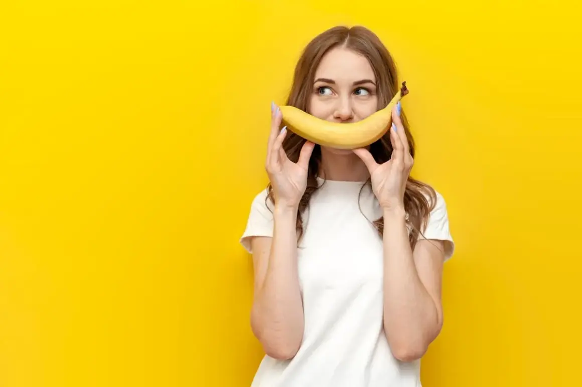 Une jeune femme tient une banane devant sa bouche, souriant. La question "la banane fait elle grossir ?" flotte dans l'air.