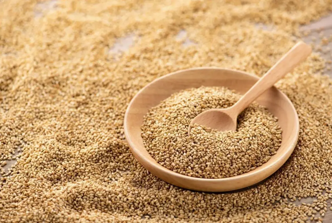 Un bol en bois rempli de graines de sésame, avec une cuillère en bois. Les graines de sésame bienfait sont une source de nutriments.