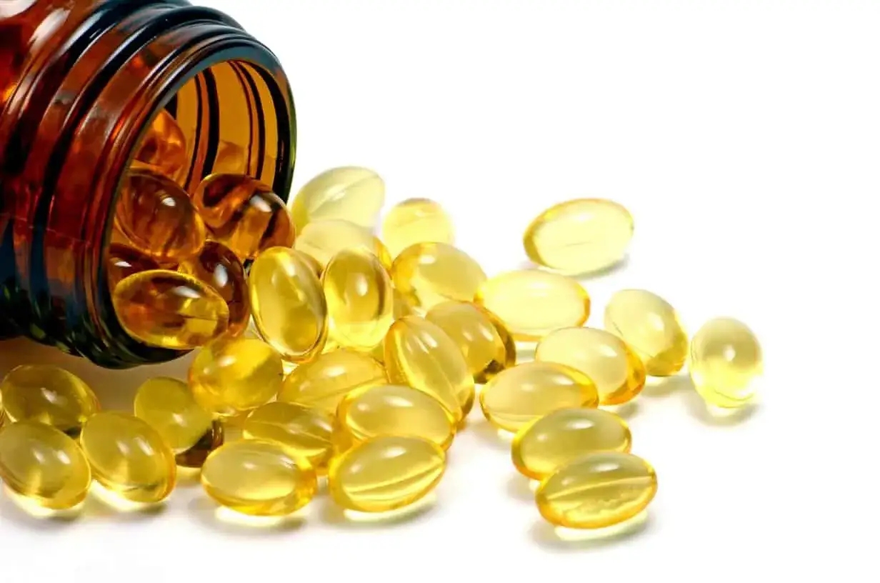 Gélules dorées renversées d'un flacon ambré, évoquant la vitamine D pour des cheveux éclatants de santé.