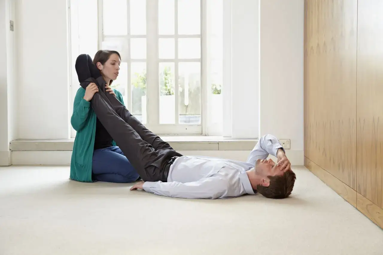 Une femme aide un homme qui semble souffrir d'un malaise vagal, en lui relevant les jambes. Un remède de grand-mère pour se rétablir.