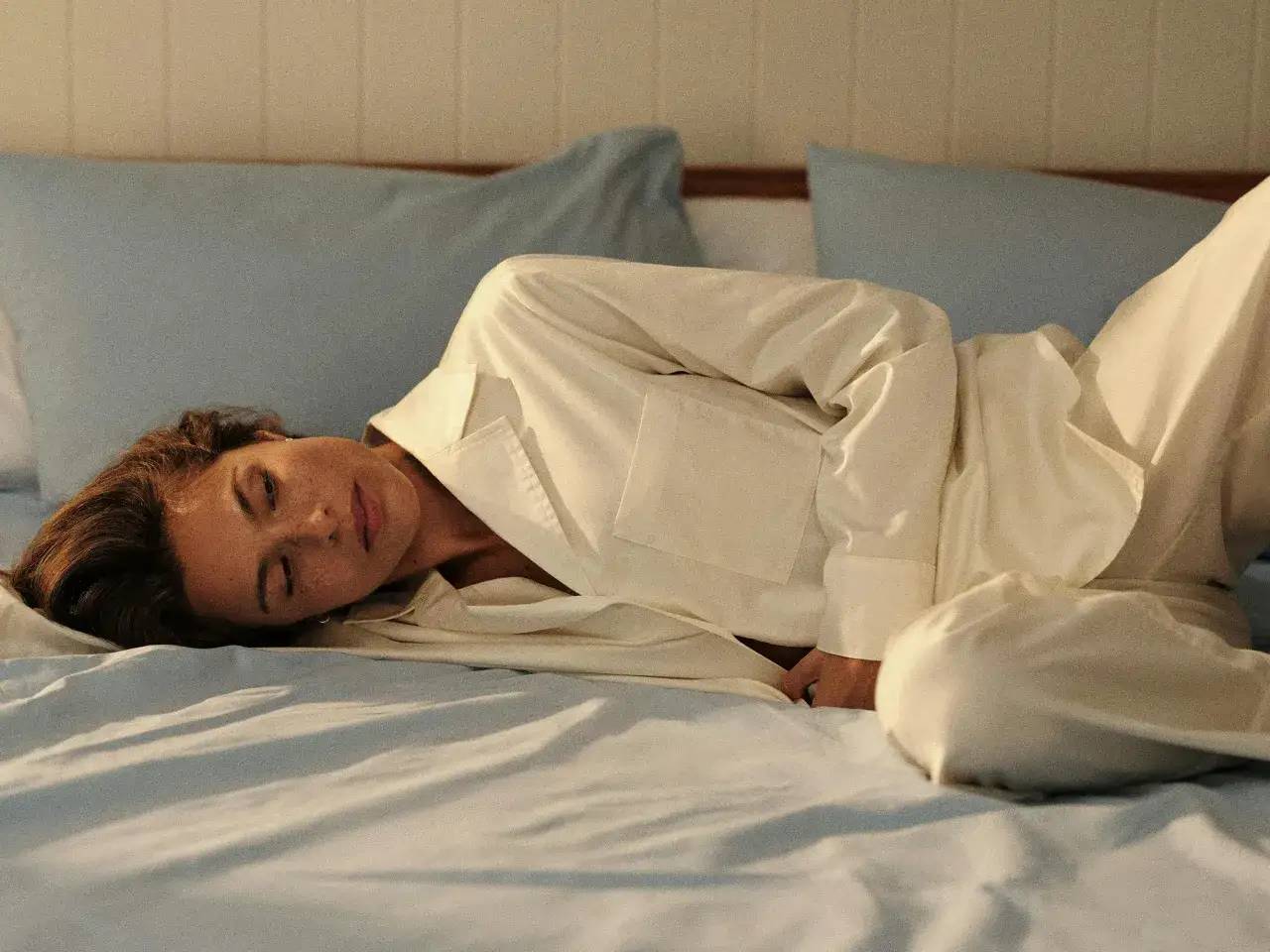 Une femme se repose sur un lit, ses yeux clos. Elle porte un pyjama blanc, peut-&ecirc;tre pour soulager les sueurs nocturnes post partum.