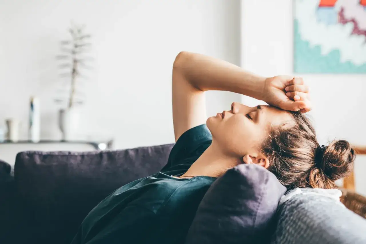 Une jeune femme repose sur un canapé, la main sur le front, l'air fatigué et ayant froid.