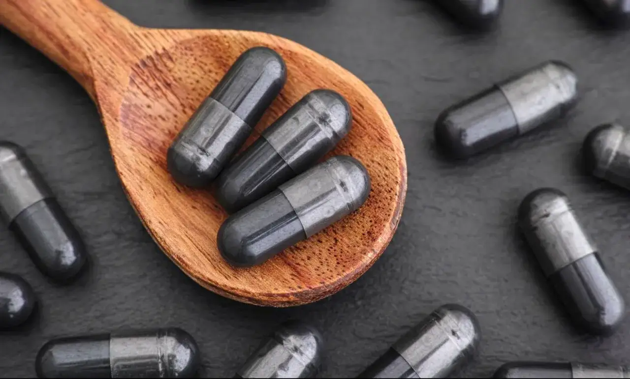 Trois gélules de charbon actif sur une cuillère en bois, prêtes pour une cure avant de dormir.