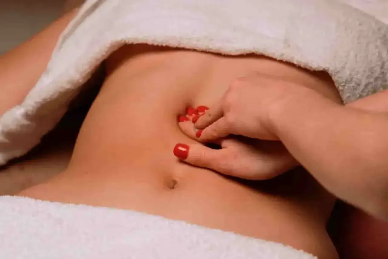 Main d'une femme avec des ongles rouges testant l'abdomen pour un diastasis. Comment savoir si vous en avez un ?