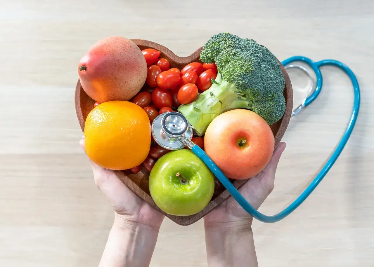 Un cœur en bois rempli de fruits et légumes frais, avec un stéthoscope. Un conseil pratique anticholestérol pour une vie saine.