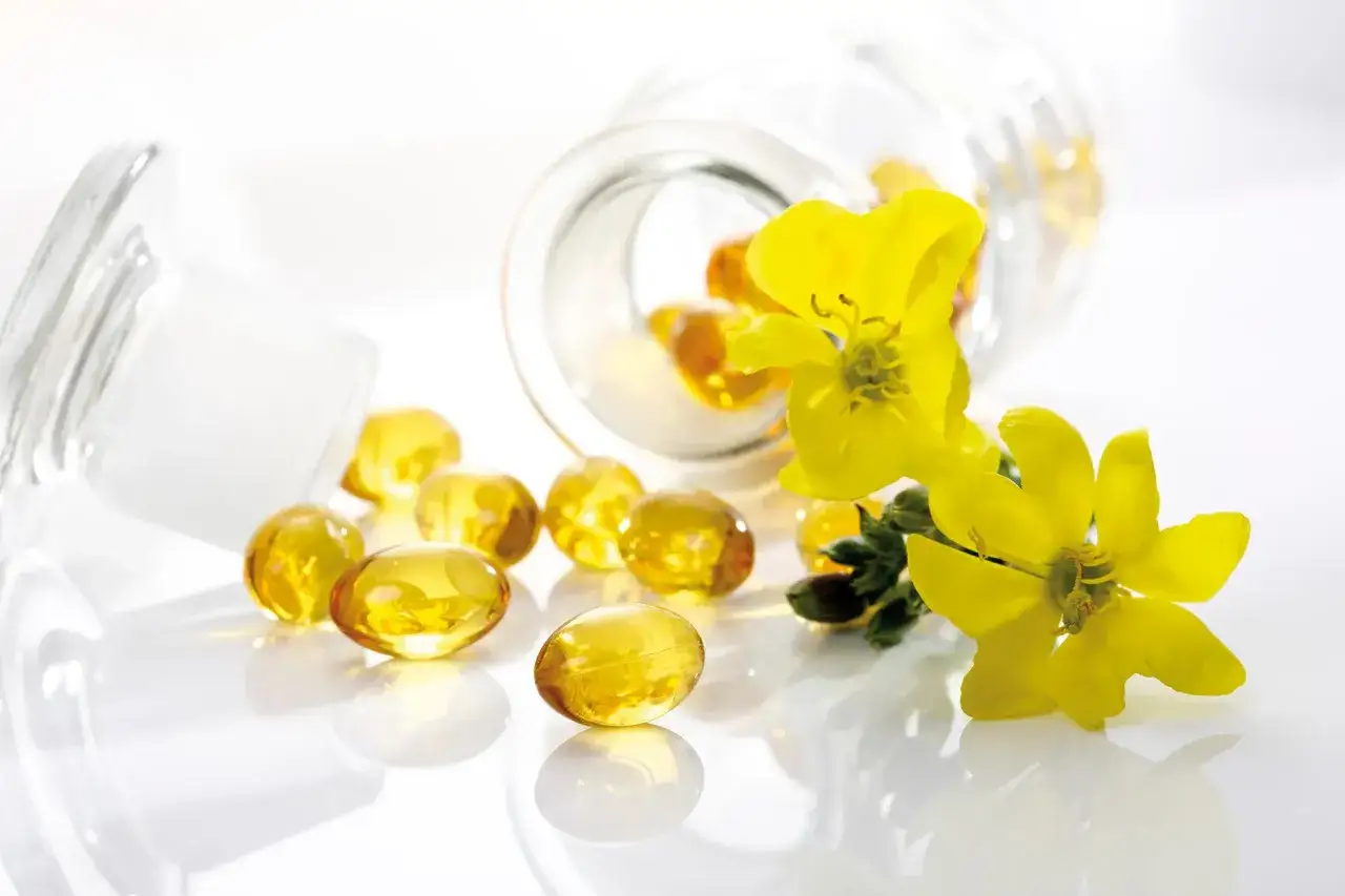 Gélules dorées d'huile de bourrache et onagre, idéales pour accompagner la ménopause, aux côtés de fleurs jaunes lumineuses.