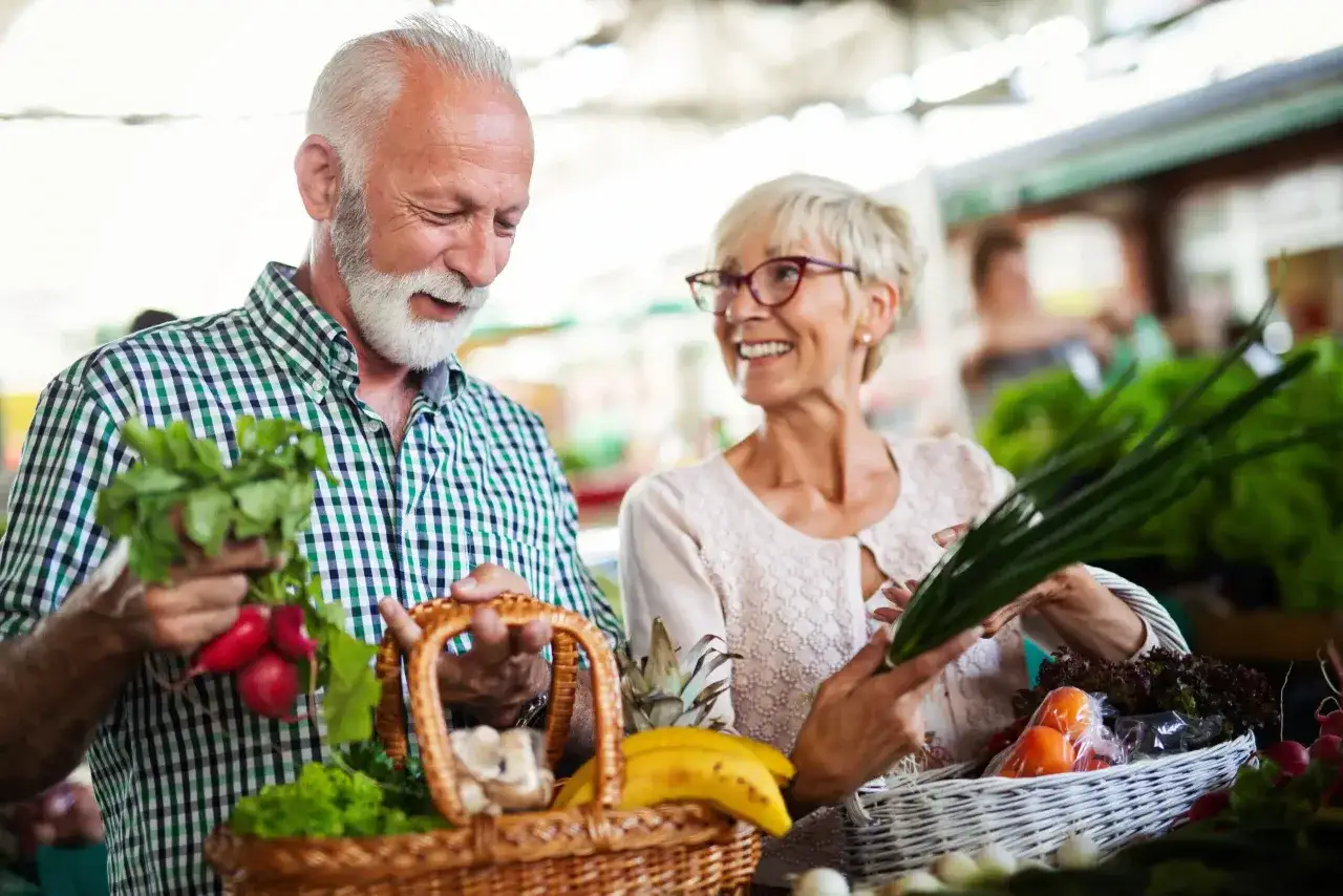 Couple âgé choisissant des aliments riches en protéines pour personnes âgées au marché : radis, oignons verts, fruits et légumes frais.