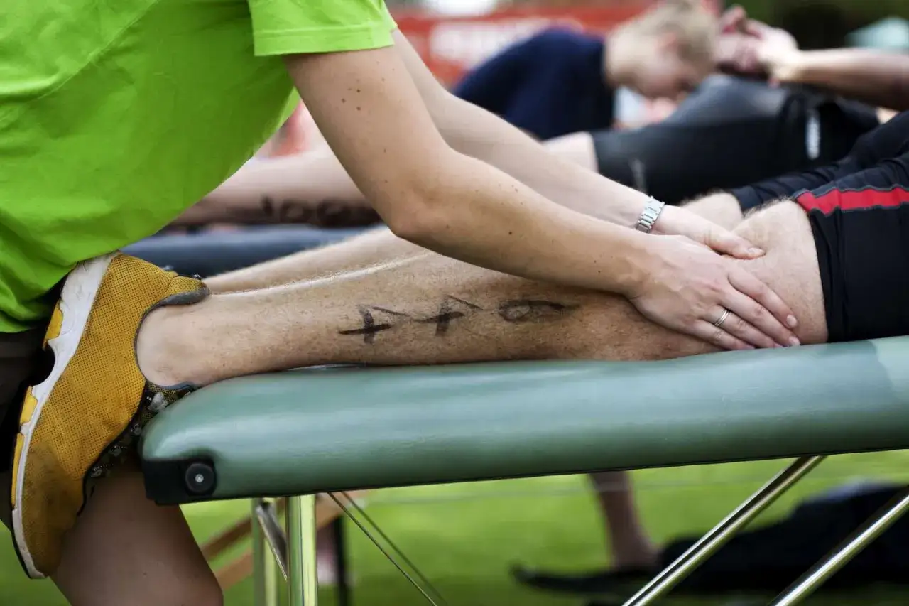 Massage pour soulager les courbatures après un effort. Un athlète est allongé sur une table de massage, une personne lui masse la jambe.