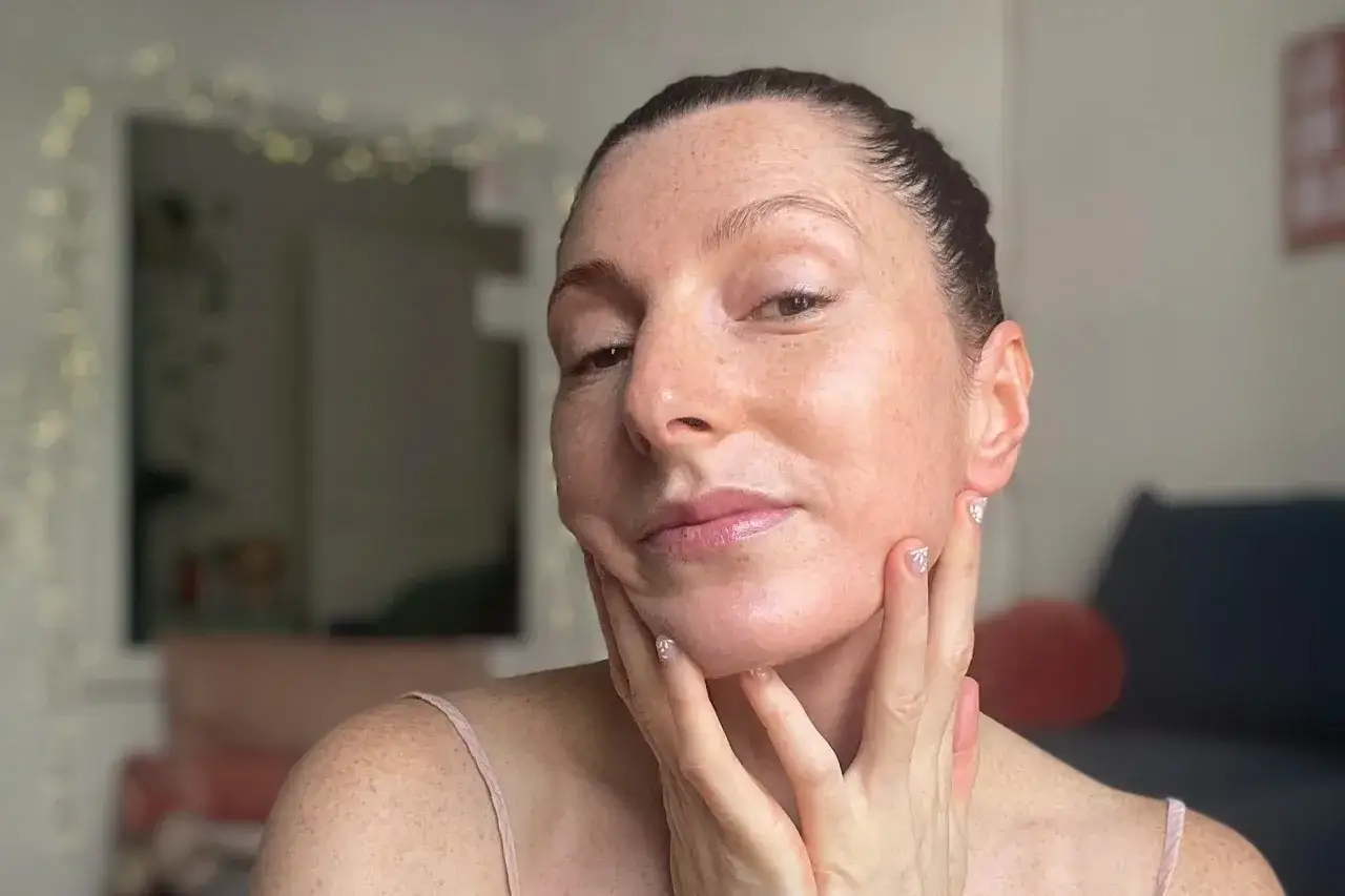 Visage d'une femme aux taches de rousseur, mains sur le menton. Elle utilise un produit à base de zinc pour sa peau, afin de réduire les rides.