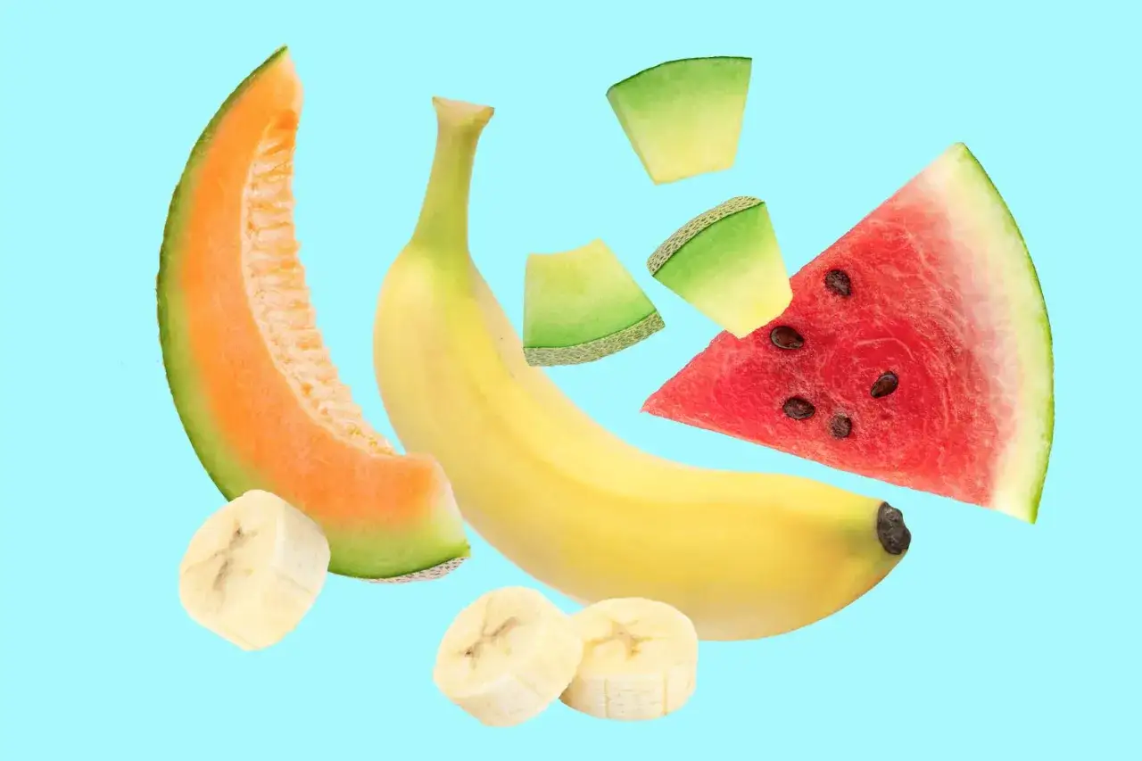 Un assortiment de fruits non acides : banane, pastèque, melon cantaloup et morceaux de banane sur fond bleu clair.