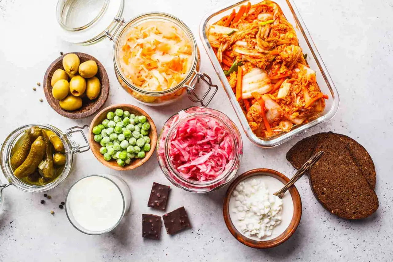 Assortiment d'aliments fermentés : choucroute, kimchi, cornichons, olives, yaourt, kéfir, pain de seigle. Un aliment fermenté à éviter ? Le chocolat noir, bien que délicieux, n'est pas fermenté.