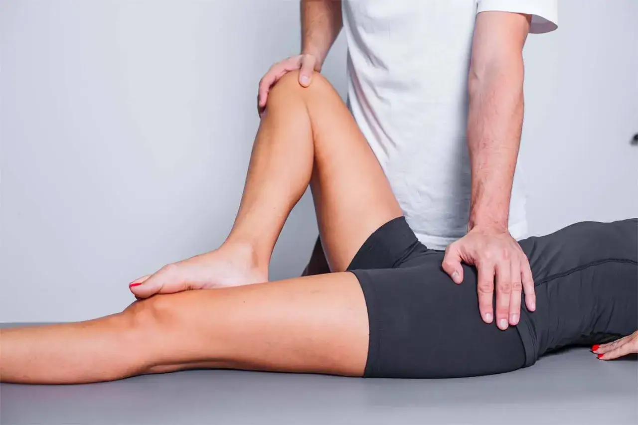 Un kinésithérapeute examine la jambe d'une patiente, cherchant la cause de sa douleur hanche et genou marche.