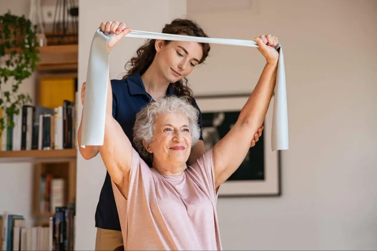 Une femme âgée fait des exercices avec une bande élastique, guidée par une thérapeute. Un traitement naturel pour la fonte musculaire.