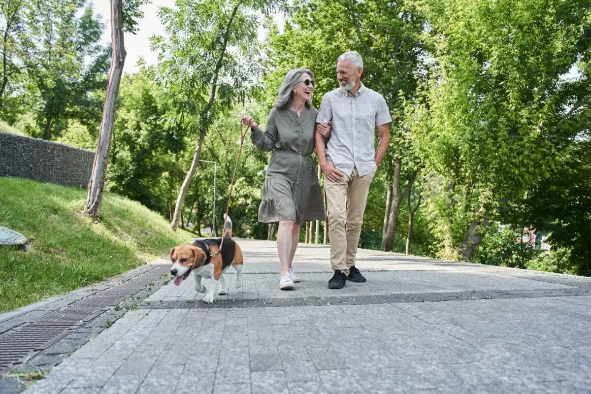 Un couple profite d'une promenade avec leur chien, une activité bénéfique malgré l'arthrose lombaire.