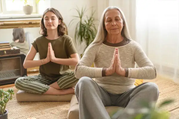 Deux femmes méditent, une jeune et une plus âgée. La méditation peut aider à gérer le stress et la prise de poids liée à la préménopause.