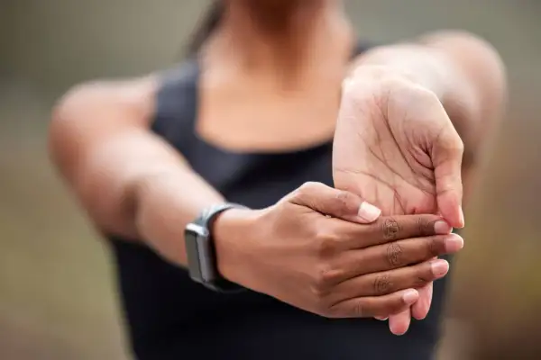 Une femme étire son poignet, peut-être pour soulager une douleur poignet externe après un effort.