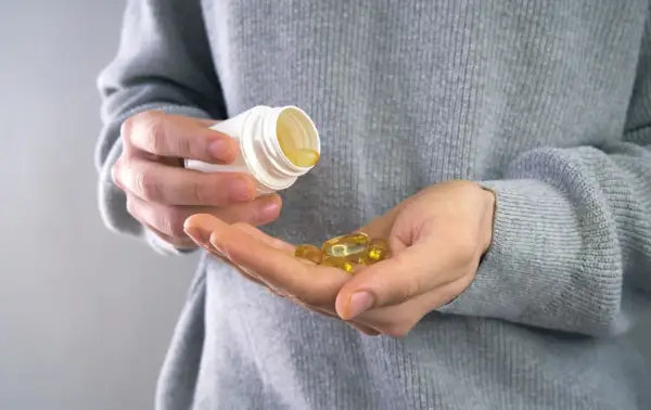 Main tenant une capsule d'huile de poisson dans sa main, prêt à prendre son complément. Avis sur les oméga 3.