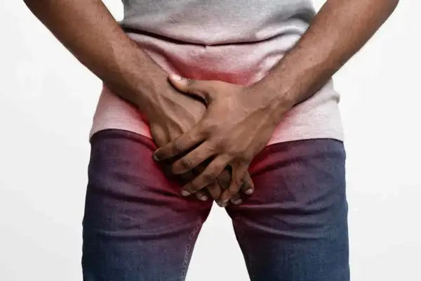 Homme tenant ses mains sur son pubis, zone rouge indiquant une douleur ou une gêne.