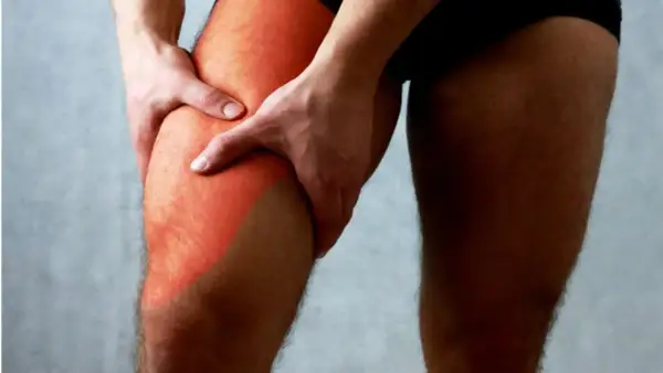 Main gauche tenant la cuisse droite, marquée d'une zone rouge symbolisant une douleur haut de la cuisse.