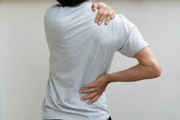 Person ressentant une douleur au haut du dos bloqué, une main sur l'épaule, l'autre sur la hanche.