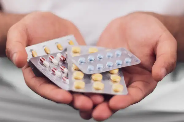 Mains tenant plusieurs plaquettes de pilules, dont des gélules rouges et blanches, des comprimés bleus et des comprimés jaunes. Que prendre avec des antibiotiques ?