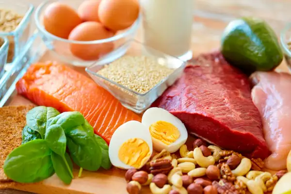 Assortiment d'aliments riches en protéines pour personnes âgées : saumon, bœuf, poulet, œufs, noix, épinards, avocat, quinoa et lait.