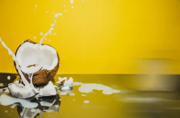 Un coco ouvert éclabousse du lait blanc sur un fond jaune vif, évoquant les nombreux lait de coco bienfaits.