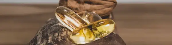 Trois capsules d'oméga 3 dorées reposent sur une noix. Quand prendre oméga 3 pour un bien-être optimal ?