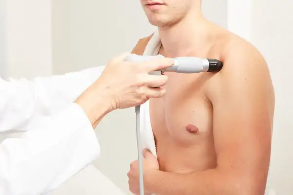 Thérapeute appliquant des ondes de choc radiales sur l'épaule d'un patient pour soulager la douleur.