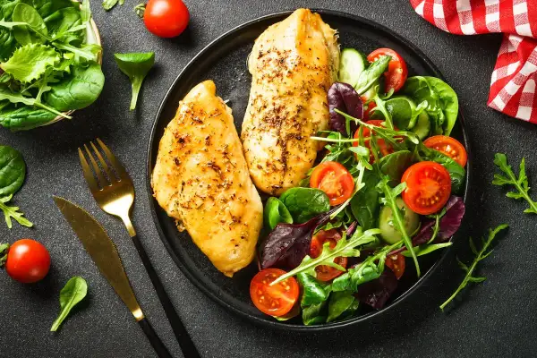Deux blancs de poulet grillés avec une salade fraîche. Un repas sain, idéal pour savoir quels aliments éviter quand on a du cholestérol.