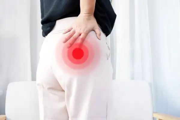 Une femme se tient le fessier droit, marqué par des cercles rouges, suggérant une douleur. La signification de cette douleur fessier droit peut varier.