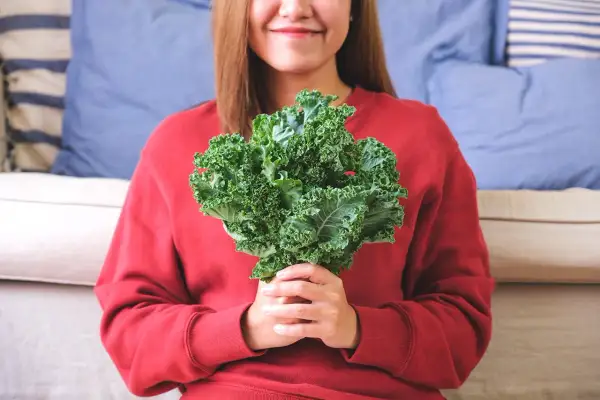 Une femme souriante tient un bouquet de chou kale, un légume aux multiples chou kale bienfaits pour la santé.