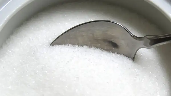 Une cuillère dans un bol de sucre blanc, rappelant les dangers du cholestérol, du sucre ou du sel pour la santé.