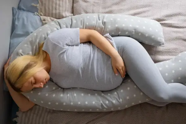 Femme enceinte dormant sur un coussin de maternité, cherchant le confort face aux douleurs ligamentaires de grossesse.