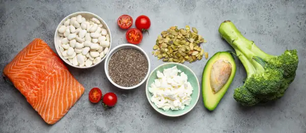 Saumon, haricots blancs, tomates, graines de chia, fromage blanc, avocat et brocoli sur fond gris.