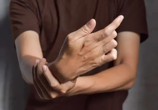 Main tenant une main, l'autre main se tient le poignet, suggérant des symptômes de fonte musculaire.