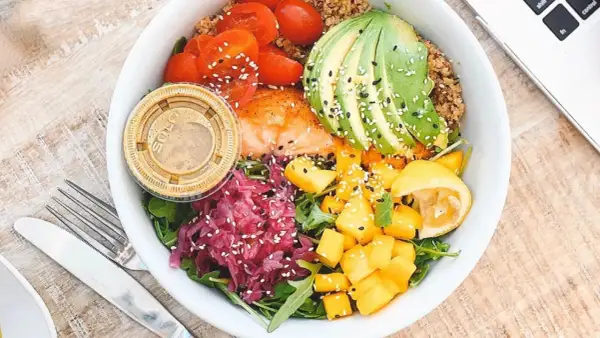 Un bol coloré avec saumon, avocat, tomates, mangue et chou rouge. Une assiette saine pour savoir comment faire baisser son taux d'insuline naturellement.