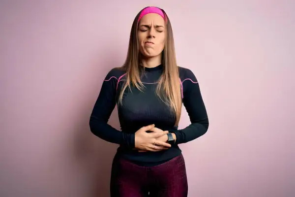 Femme en tenue de sport, mains sur le ventre, grimace de douleur. Elle a des douleurs de règles mais pas de règles.