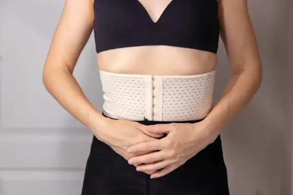 Ceinture de resserrage du bassin, beige, avec fermeture à crochets, portée sous un soutien-gorge noir.
