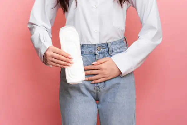 Une femme tient une serviette hygiénique, le ventre douloureux, symbolisant la douleur de règle sans règle.