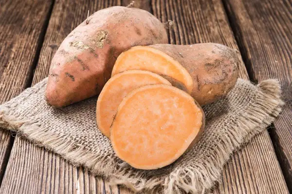 Patates douces entières et tranchées sur une toile de jute. Un aliment sain, faible en calories, parfait pour une alimentation équilibrée.
