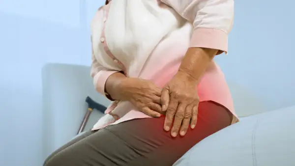 Une personne âgée ressent une douleur à la hanche, peut-être due à une ancienne blessure de course à pied. Une canne est visible à proximité.