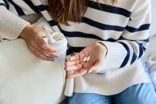 Une femme tient des comprimés dans sa main, peut-être pour lutter contre la fatigue. Le collagène est une option.