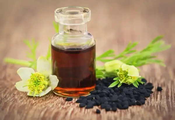 Flacon d'huile de nigelle, graines noires et fleurs. Un remède naturel pour la fonte musculaire.