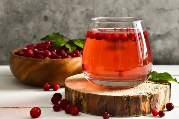Verre de jus de cranberry, fruit réputé pour aider contre l'infection urinaire. Baies rouges dans un bol en bois.