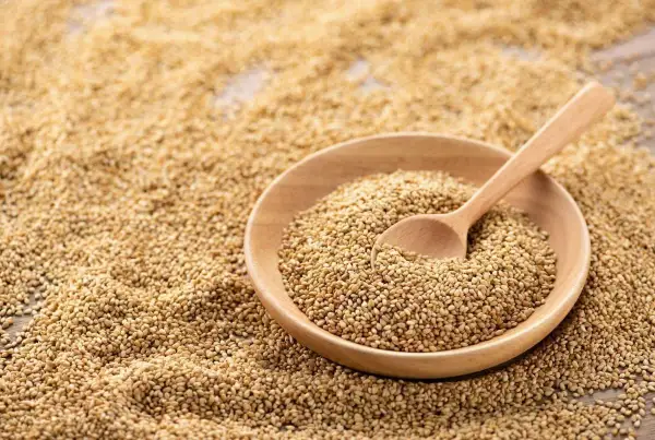 Un bol en bois rempli de graines de sésame, avec une cuillère en bois. Les graines de sésame bienfait sont une source de nutriments.