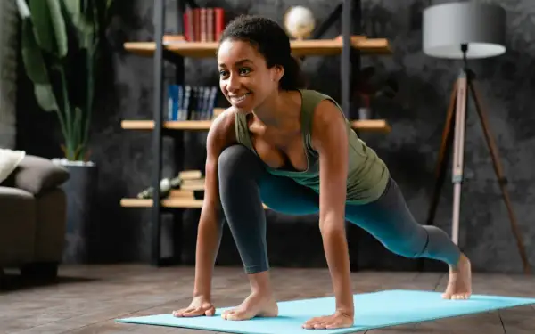 Jeune femme souriante en plein grand écart latéral sur un tapis de yoga bleu, dans un salon cosy.